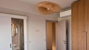 Un dormitorio con cama, armario de madera, baño con espejo y lavamanos, y lámpara de techo tejida.