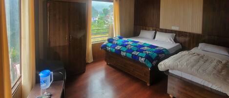 A bedroom with two beds, wooden flooring, a desk with a chair, a ceiling fan, and a window with curtains.