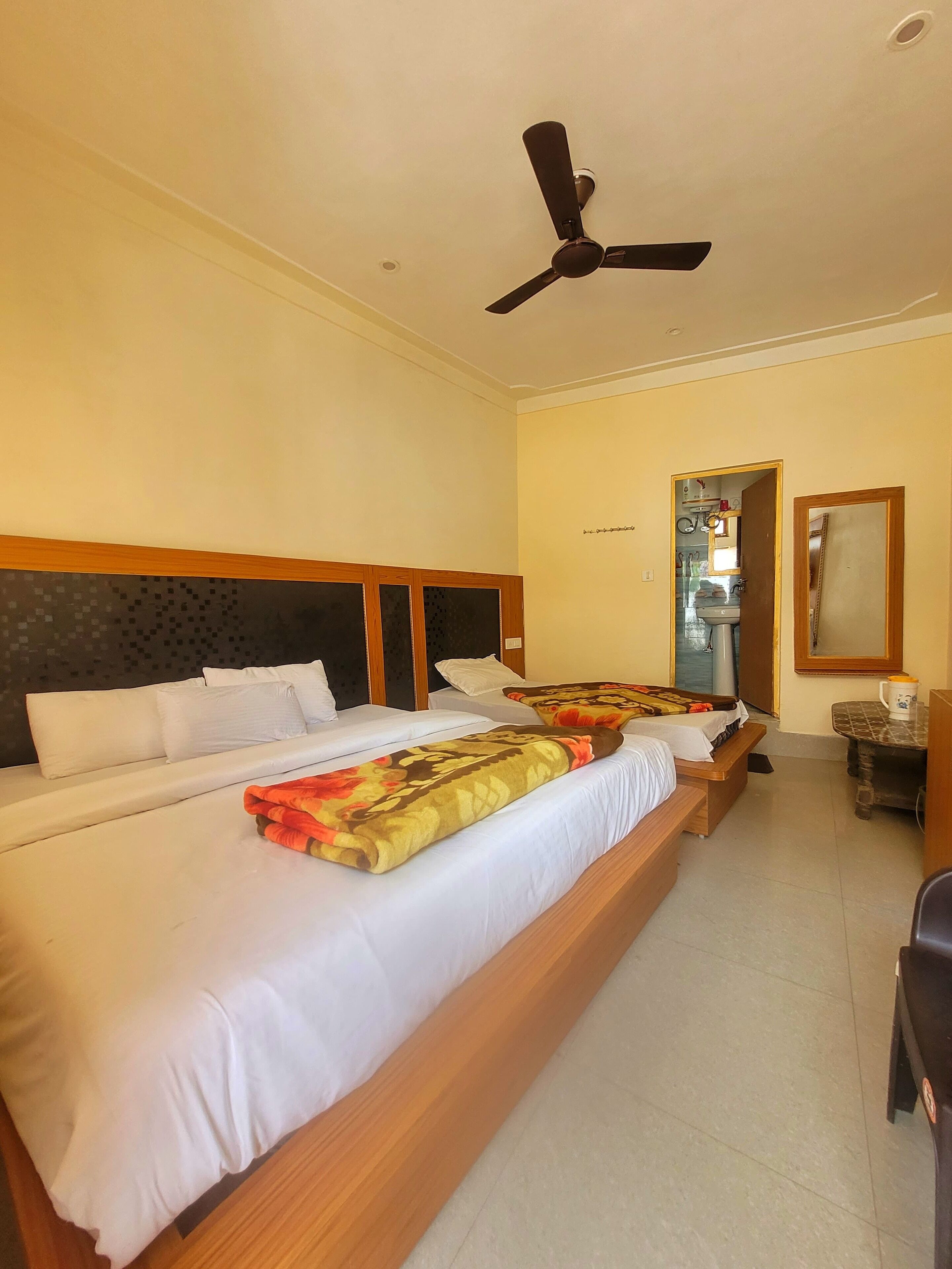 A double bed with a patterned blanket, a bedside table with a cup, and a ceiling fan.