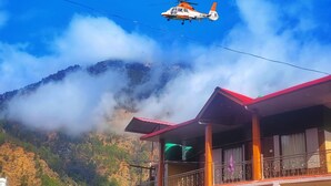 A helicopter flying over a building with a balcony, surrounded by mountains and clouds. - Shivlok Hotel  (Ukhimath)