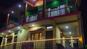 A two-story hotel with a balcony on the upper floor, a sign indicating rooms are available, and a visible entrance with a checkered floor pattern. - Shivlok Hotel  (Ukhimath)
