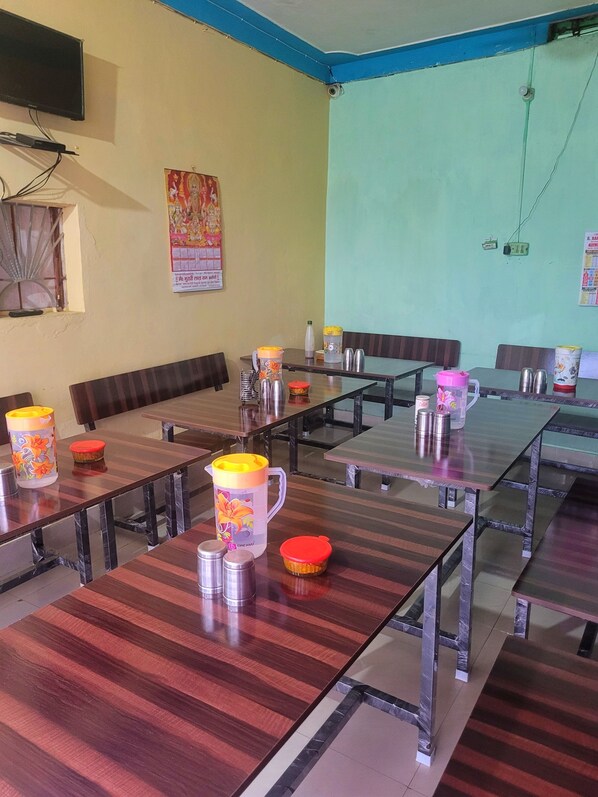 A conference room with multiple tables and chairs, equipped with stainless steel water pitchers and thermoses. - Shivlok Hotel (Ukhimath)