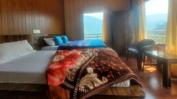 A hotel room with a bed, a chair, a table, and a window with a view. - Shivlok Hotel  (Ukhimath)