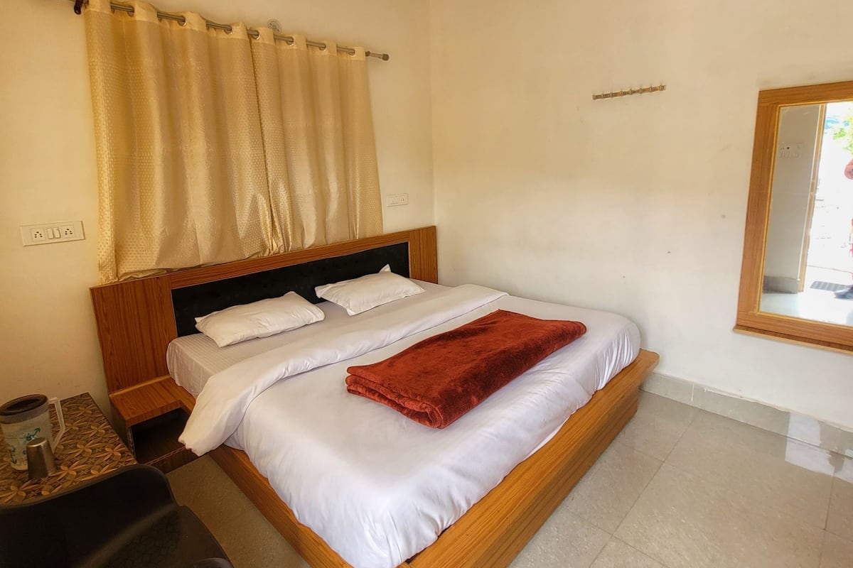 Ein Hotelzimmer mit einem Einzelbett, einem Holz-Kopfteil, einem Deckenventilator, einem kleinen Tisch mit Stuhl und einem Fenster mit Vorhängen.