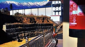 A balcony with a view of snow-capped mountains, a railing with a flag, and a fire extinguisher on the wall. - Shivlok Hotel  (Ukhimath)