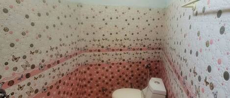 Ein kleines Badezimmer mit Toilette, einem roten Eimer und Wandverkleidung mit Muster.