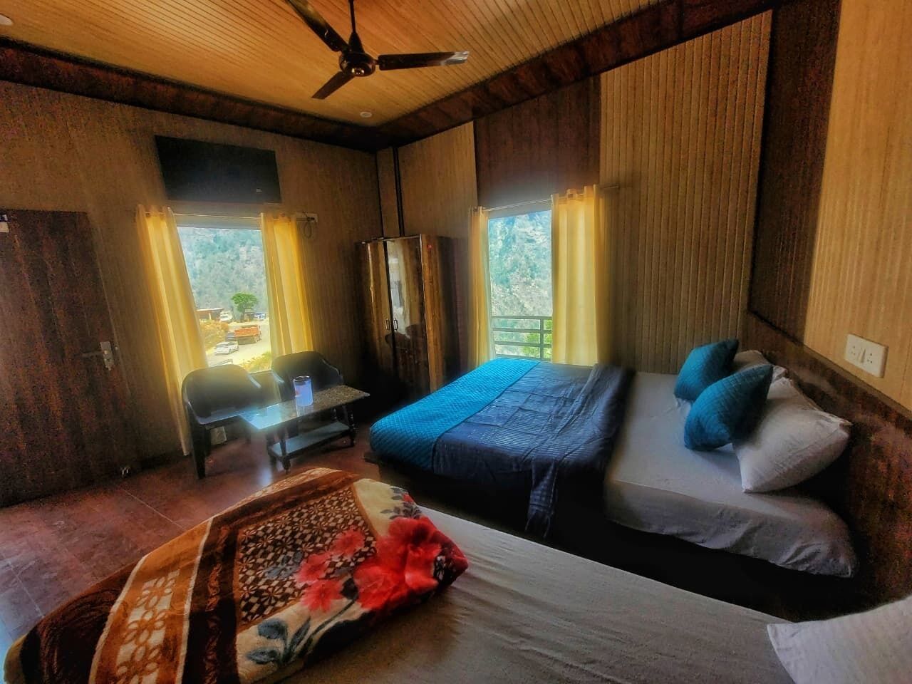 A room with two beds, a desk, a chair, and a ceiling fan.