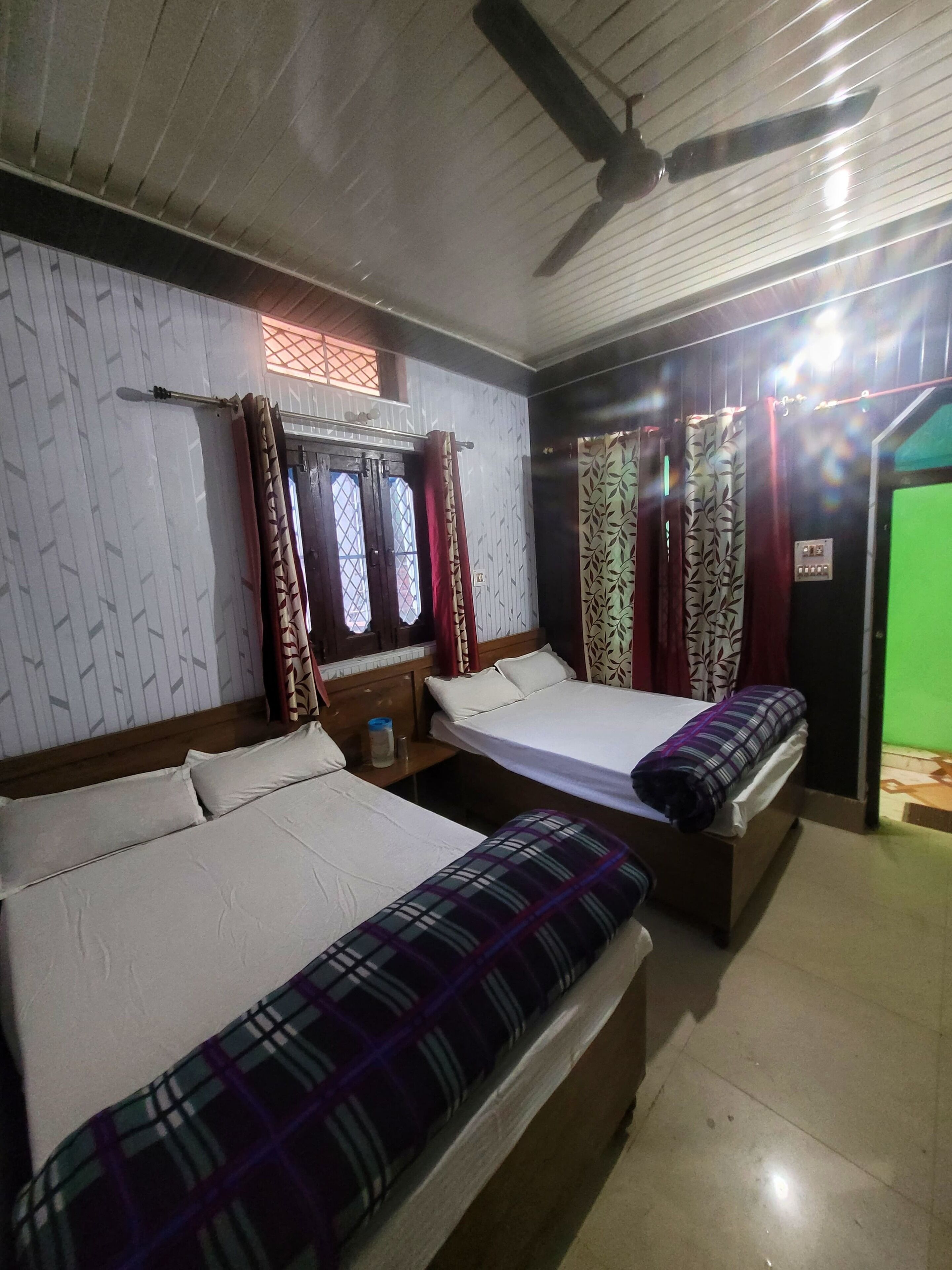 A room with two beds, a ceiling fan, and a green door.