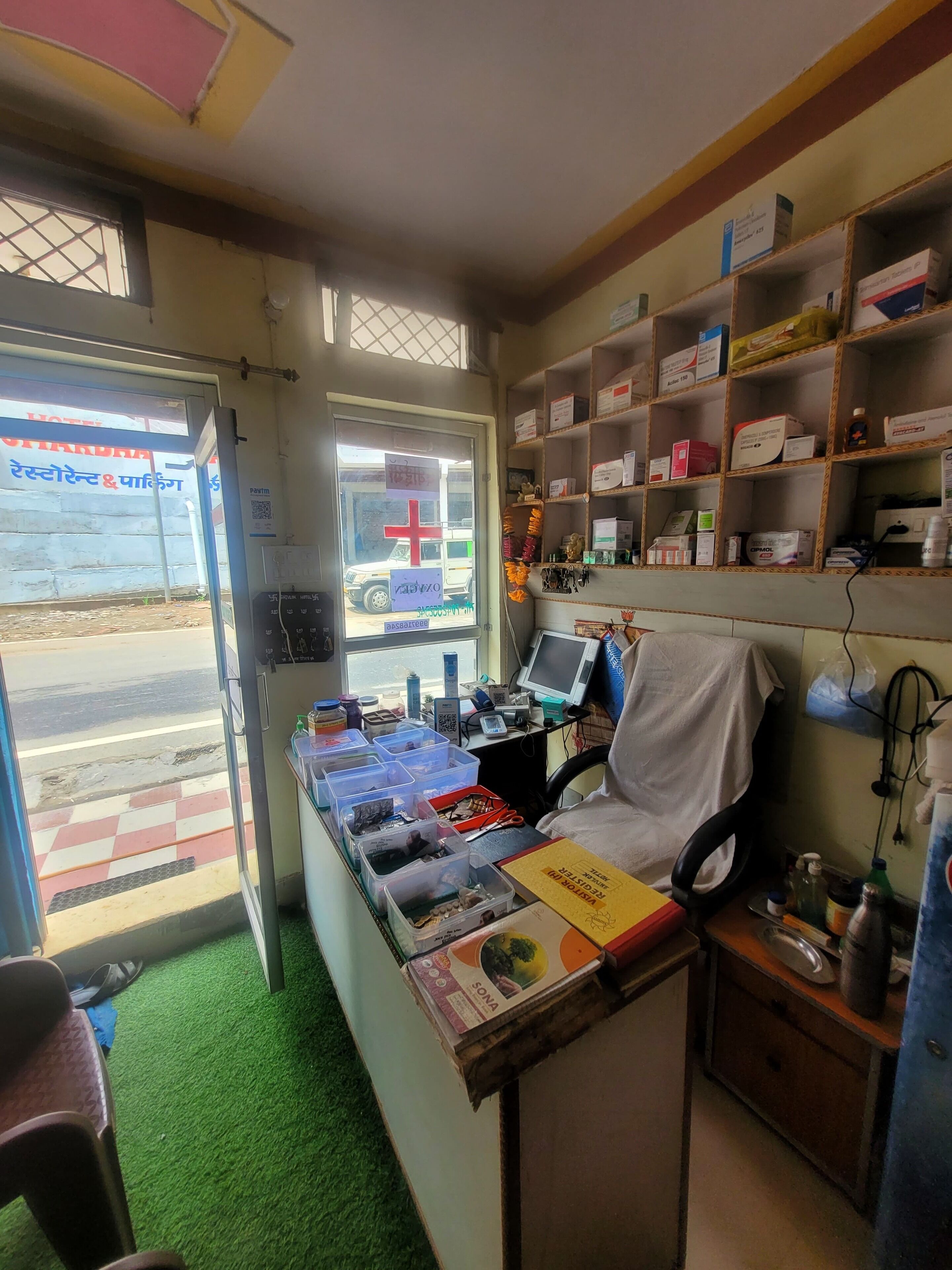 A small, cluttered room with a desk, shelves of medical supplies, a chair, and a window with a view of a street.