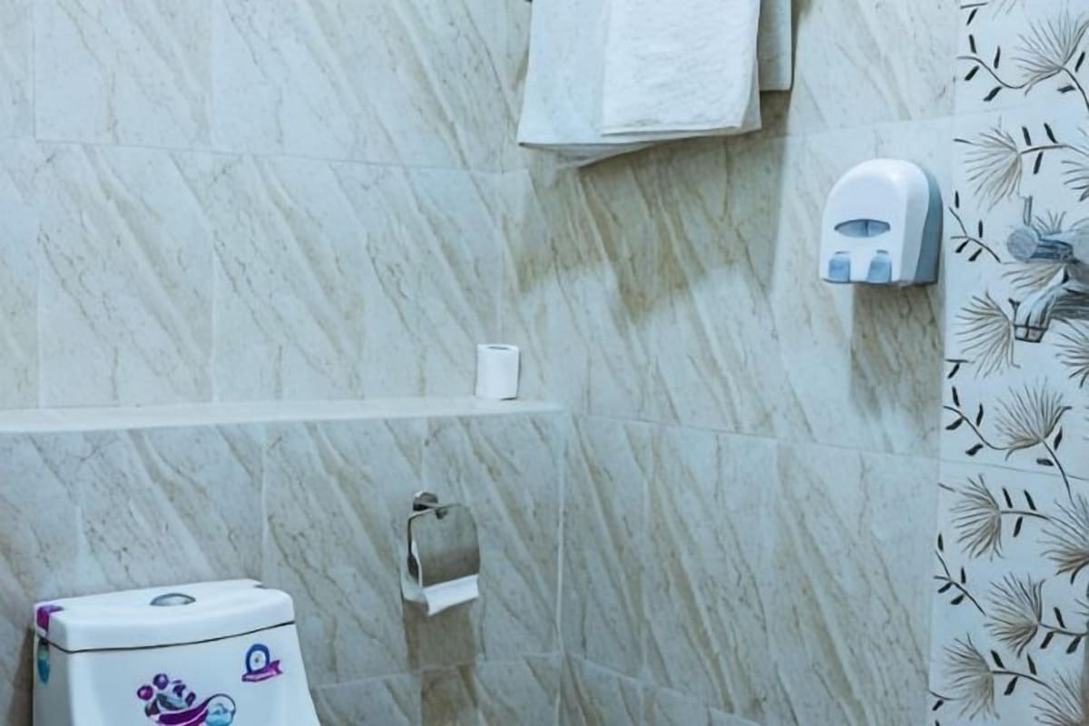 A bathroom with a marble wall, a toilet with a decorative lid, a paper towel dispenser, and a towel rack.