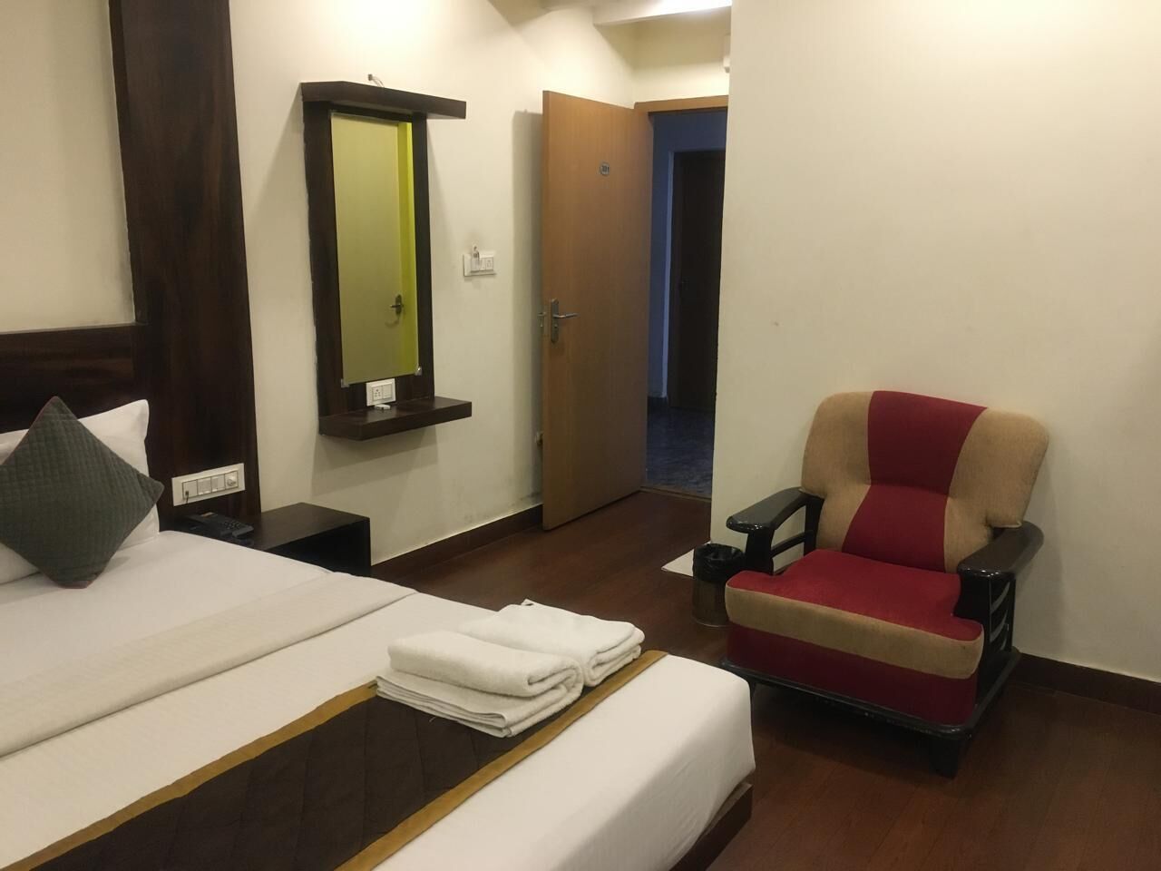 Una habitación de hotel con cama, una silla, un espejo y una puerta que da a otra estancia.