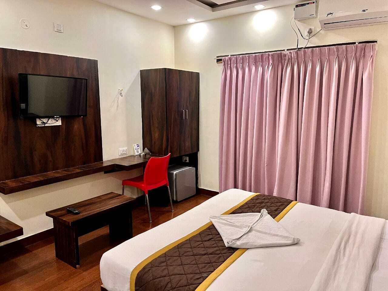 A hotel room with a bed, a desk, a chair, a TV, and a wardrobe.