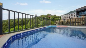 A swimming pool with a tiled edge, surrounded by a metal fence, and a building with multiple windows in the background. - Geoje Piscina Pool Villa (Geoje)