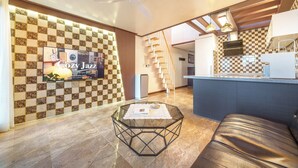 A modern living room with a glass coffee table, a leather sofa, a kitchen with checkered backsplash, and a staircase. - Geoje Piscina Pool Villa (Geoje)