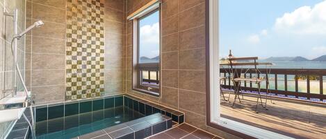 A bathroom with a glass-enclosed shower, a patterned wall, and a view of a balcony with outdoor furniture.