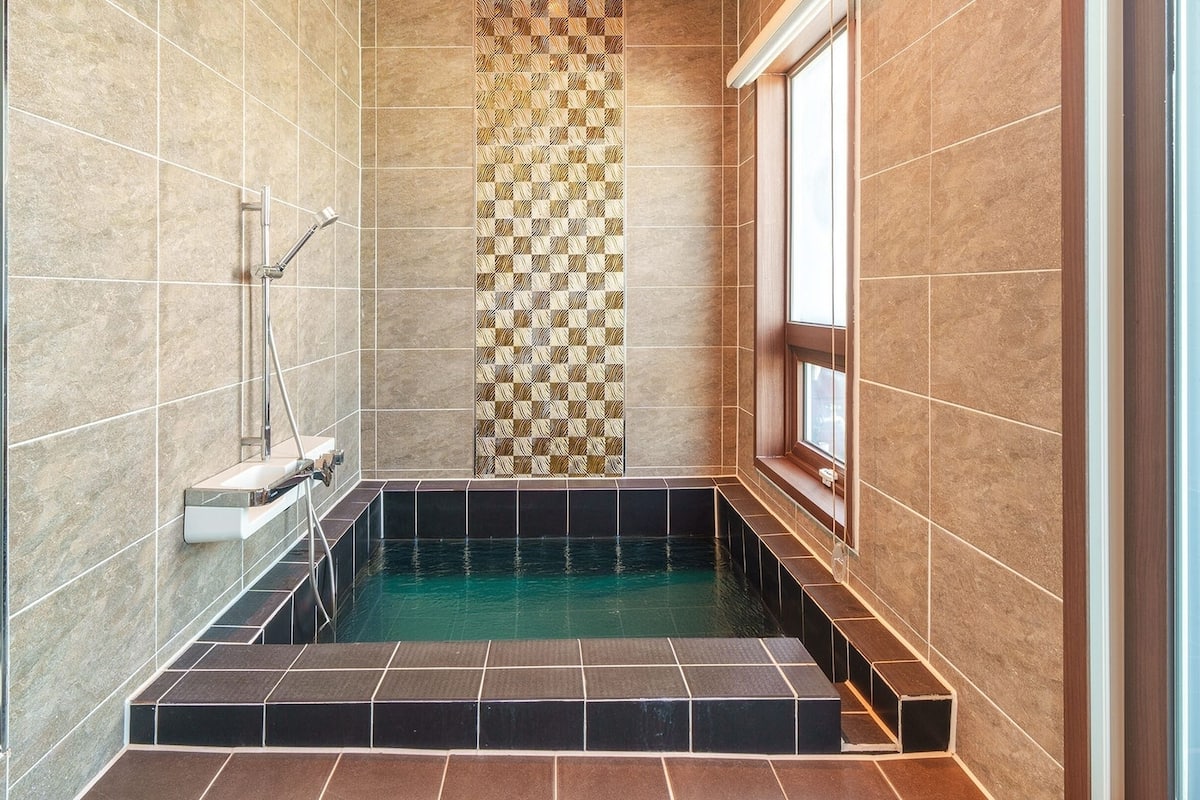A small, modern bathroom with a built-in bathtub, a shower, and a window.
