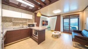 Cuina moderna amb microones integrat, un rentaplat i una petita illa. Hi ha una zona de dinar amb taula i cadires, i un gran finestral amb vista al mar.