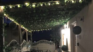 An outdoor patio area with a table and chairs, a decorative fence, and string lights. - Old Thatch Bambers Green (Bishop's Stortford)