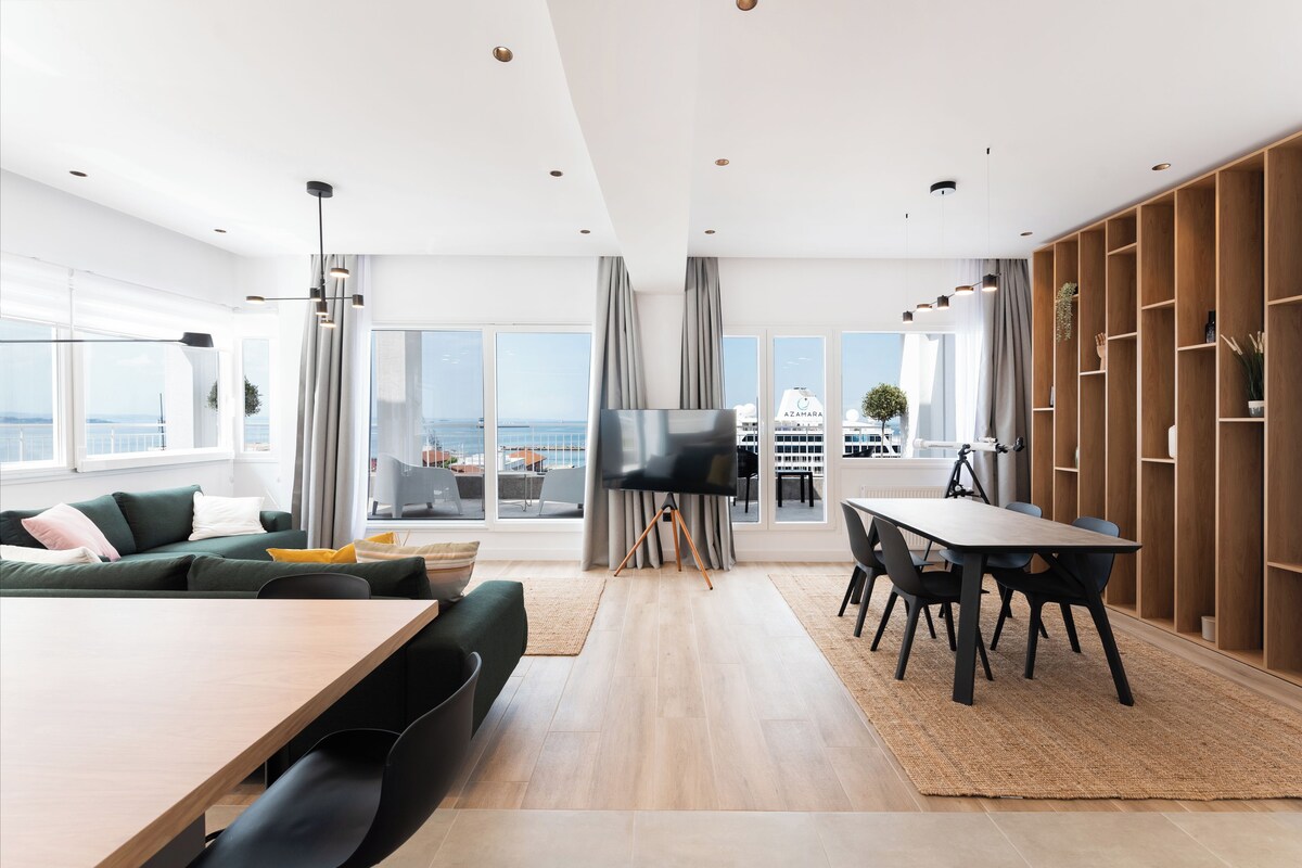 Una sala de estar moderna con un televisor grande, un comedor y vistas al mar.