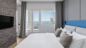Ein modernes Schlafzimmer mit einem großen Bett, einem Flachbildfernseher und Meerblick durch große Fenster.