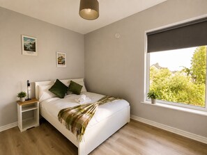 Une chambre à coucher avec un lit, une table de chevet avec une lampe, une fenêtre donnant sur un beau paysage et deux tableaux accrochés au mur.
