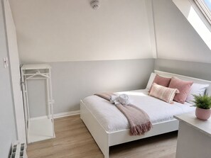 A bedroom with a bed, a bedside table with a plant, a white wardrobe, and a ceiling light.