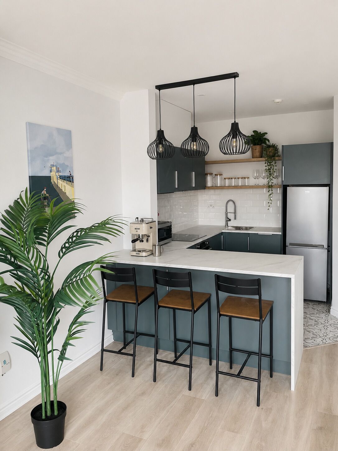 A modern kitchen with a central island, bar stools, pendant lights, and a potted plant.