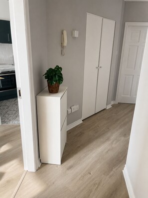 Une pièce avec une armoire blanche, un petit meuble blanc, une plante en pot et un interrupteur sur le mur.