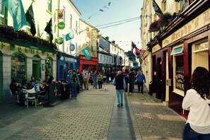 A bustling street with shops and cafes, people walking, and outdoor seating areas.