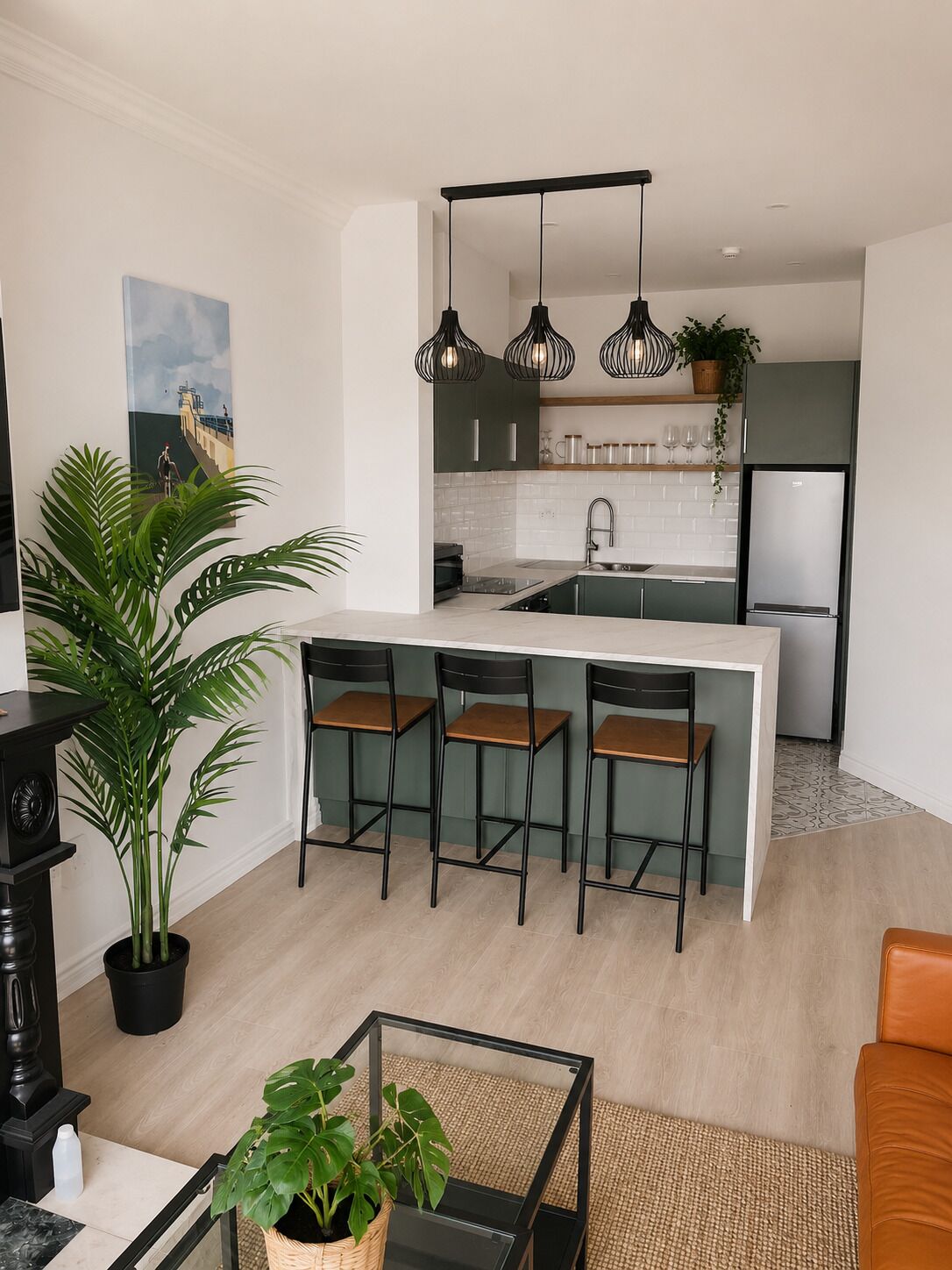 A modern kitchen with a central island, bar stools, pendant lighting, and a refrigerator.