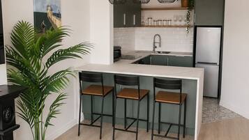 A modern kitchen with a central island, bar stools, pendant lighting, and a refrigerator.