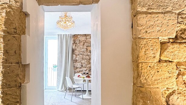 Porta de entrada para uma sala de jantar com parede de pedra, cortinas brancas e um candelabro.
