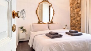 Quarto com cama, mesa de cabeceira, espelho e parede de pedra.