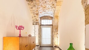 Um corredor com parede de pedra, um armário de madeira com candelabro rosa e uma garrafa verde.