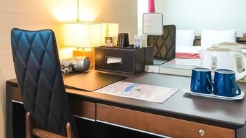 Ein Hotelzimmer mit einem Holztisch, einem schwarzen Stuhl, einer Lampe, einem Telefon, einer Kaffeemaschine und einem Tablett mit zwei blauen Tassen.