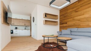 Un salon moderne avec un canapé bleu clair, deux petites tables rondes en bois, un tapis en peau de vache, un mur d’accent en bois et une cuisine en arrière-plan.