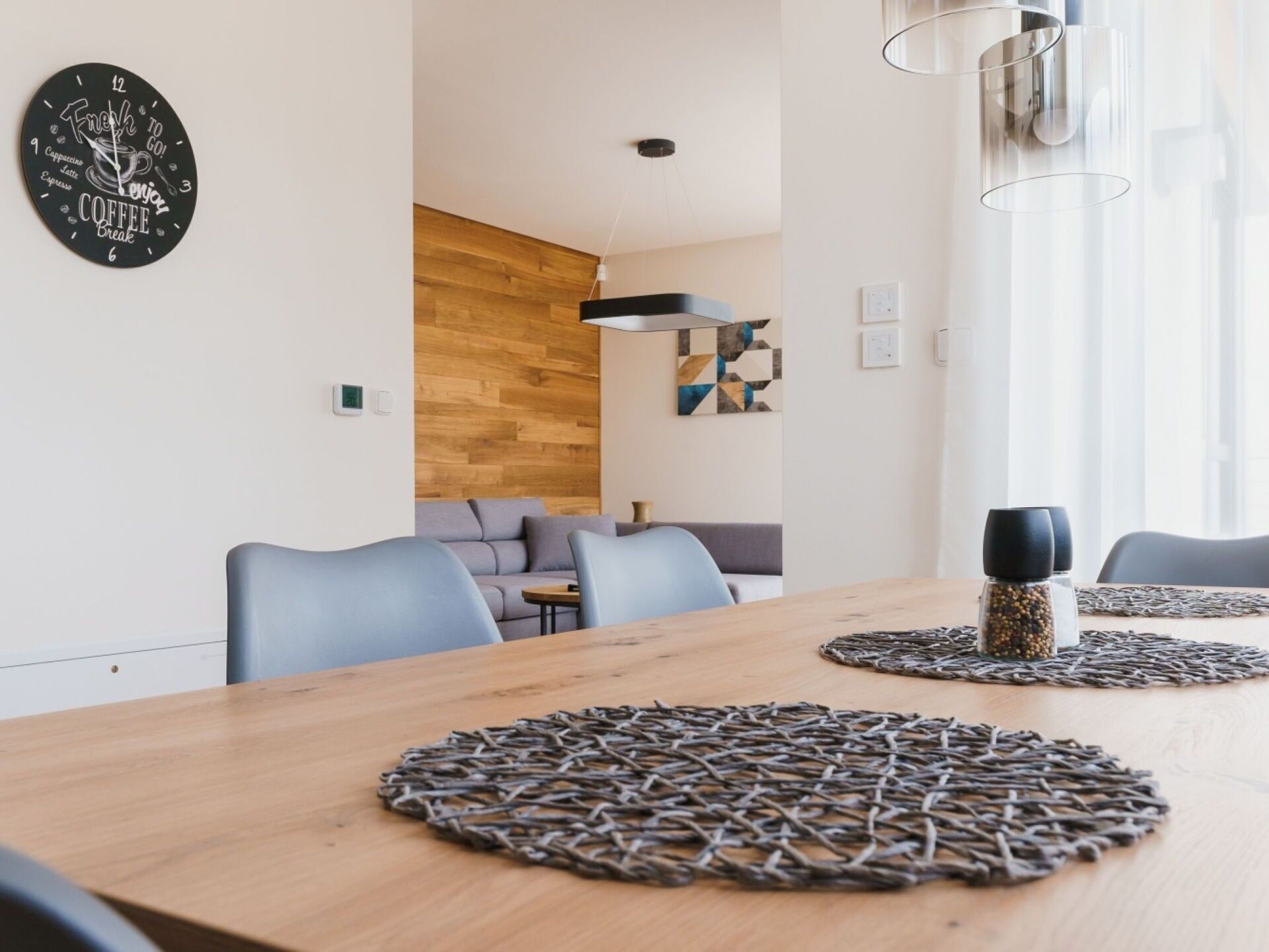 A modern dining area with a wooden table, two round coasters, and a wall clock with a coffee theme.