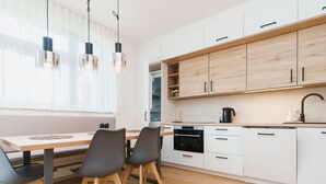 Une cuisine moderne avec des armoires blanches, un plan de travail en bois et un four encastré. On y trouve deux chaises noires et une table à manger en bois.