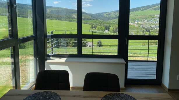 A room with large windows offering a view of green fields and hills. - Beautiful apartment for 5 people with WIFI, TV and balcony (Klášterec Nad Ohrí)