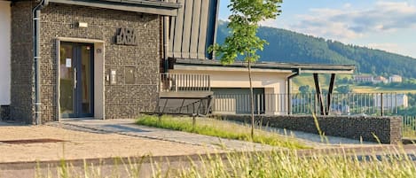 A modern building with a stone facade, a visible entrance, and a view of a river and mountains in the background.