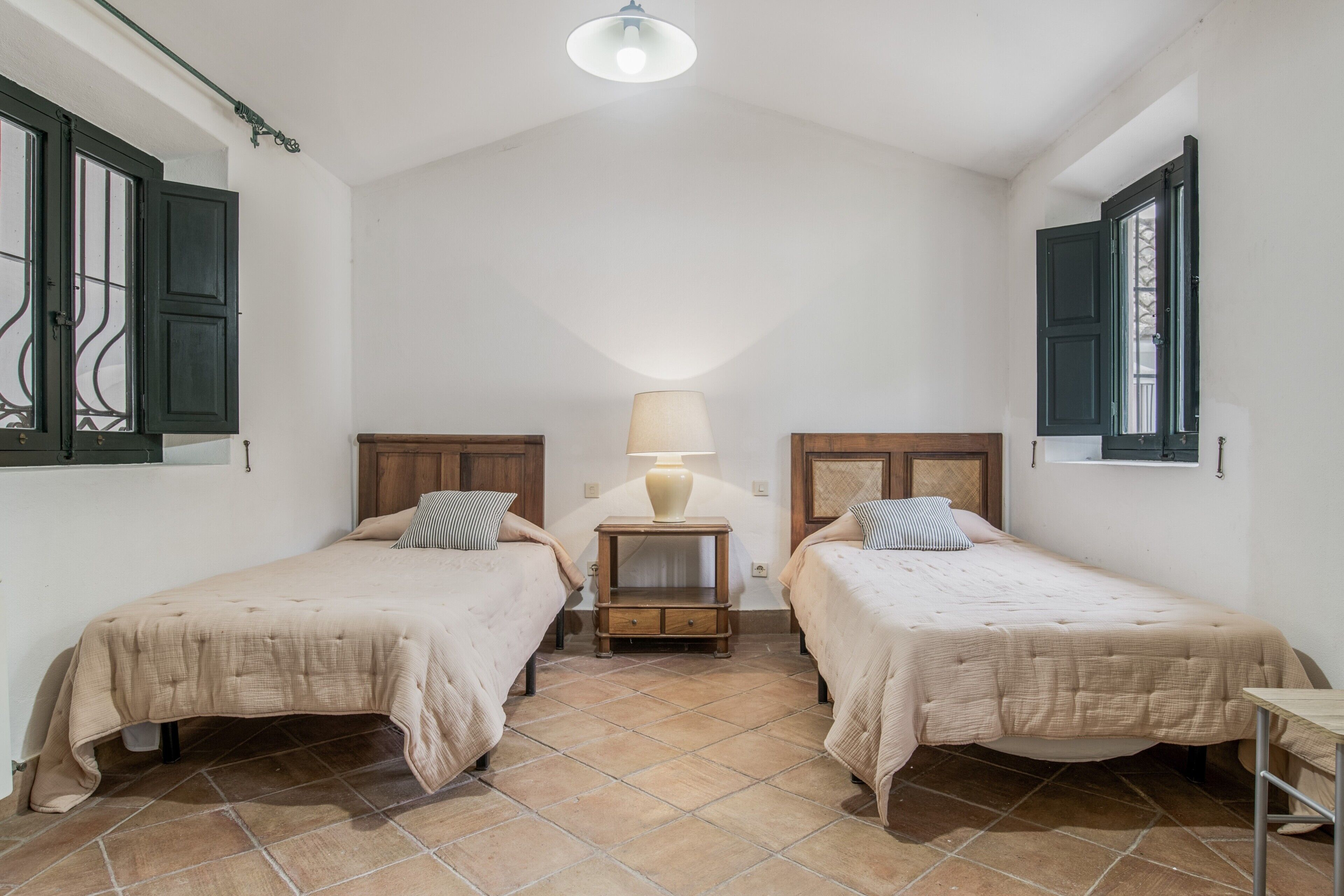 Un dormitorio con dos camas, una mesita de noche, una lámpara y una ventana con contraventanas.