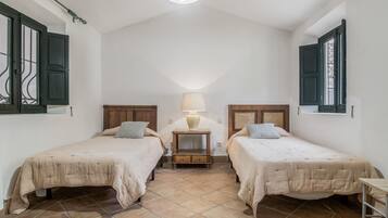 Un dormitorio con dos camas, una mesita de noche, una lámpara y una ventana con contraventanas.