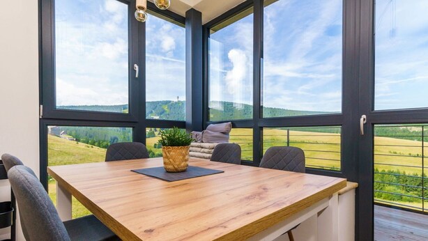 A dining area with a wooden table, four chairs, a potted plant, and a view of green fields through large windows. - Cosy apartment for 6 guests with WIFI, TV and balcony (Klášterec Nad Ohrí)