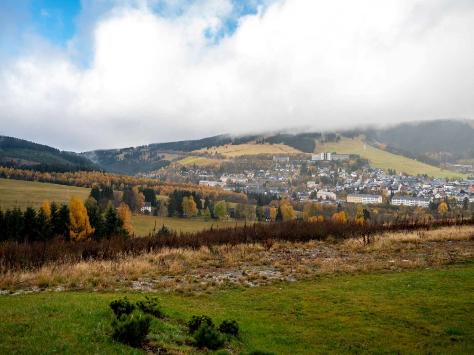 Una cittadina situata in una valle, con edifici residenziali e commerciali, circondata da colline e foglie autunnali.