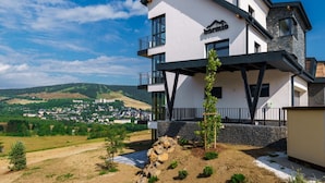 A modern two-story building with a balcony, a view of a town in the background, and a clear sky.