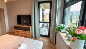 A bedroom with a bed, a TV on a wooden dresser, a window with a view of the outdoors, and a vase with flowers on the windowsill. - Cosy apartment for 4 guests with WIFI, TV and terrace (Klášterec Nad Ohrí)