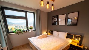 A bedroom with a large bed, a wooden dresser, a window with a view, and wall art. - Cosy apartment for 4 guests with WIFI, TV and terrace (Klášterec Nad Ohrí)