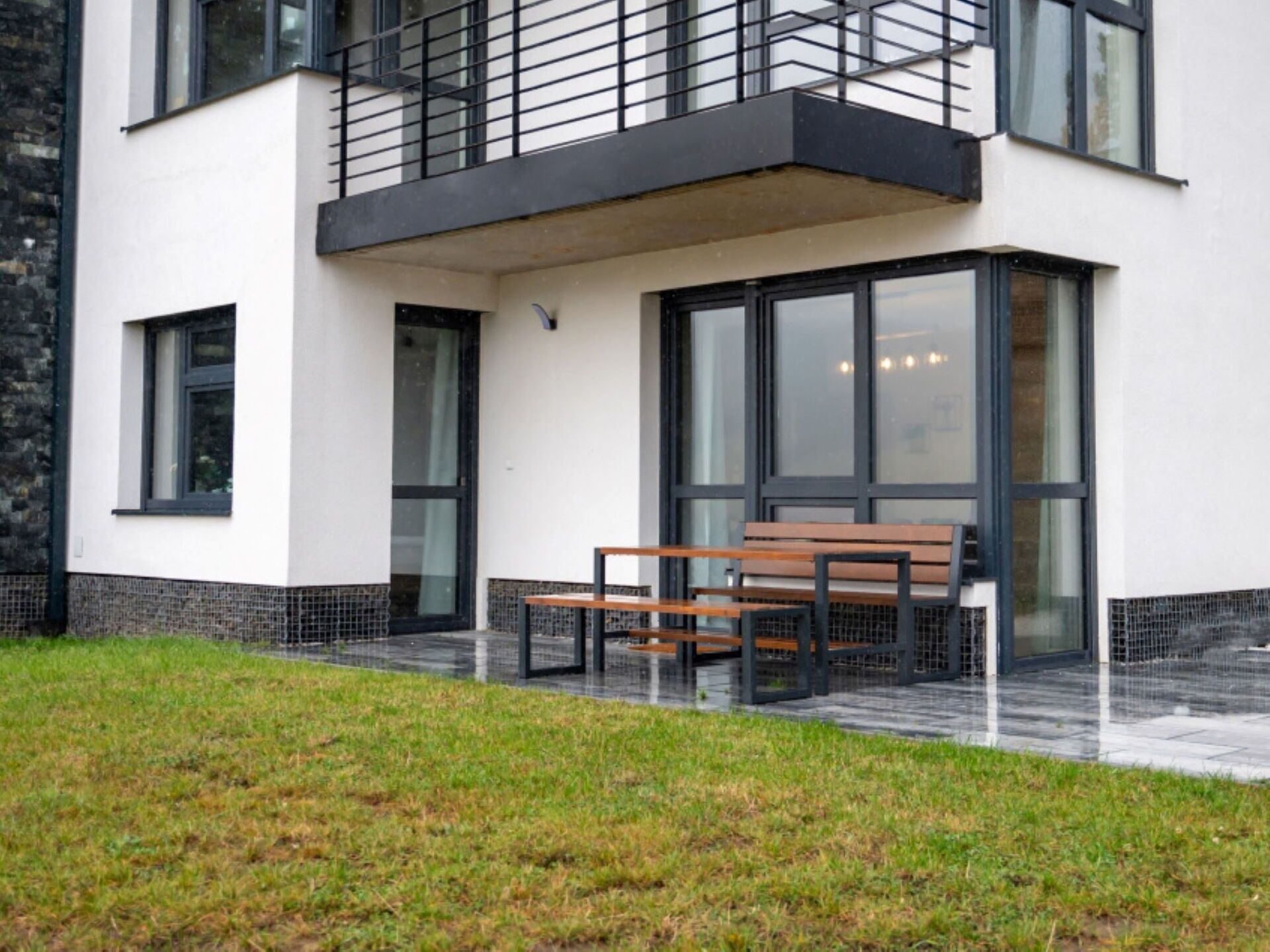 A modern building with a balcony, large windows, and a bench outside.