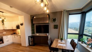 A modern kitchen with wooden cabinets, a dining area with a wooden table and chairs, and a large window with a view of the countryside. - Cosy apartment for 4 guests with WIFI, TV and terrace (Klášterec Nad Ohrí)
