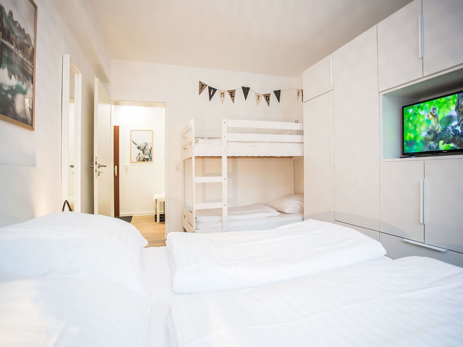 A bedroom with two beds, a bunk bed, a television, and a door leading to another room.